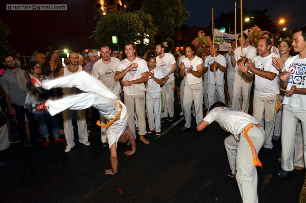 Capoeira on a closed street at night: one body inverted, one body ducking, twenty people forming a ring. The timing is everything and it happens faster than you expect.