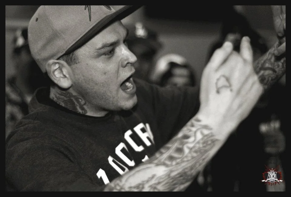 Neck tattoo, sleeve, fist raised mid-delivery — a portrait of someone entirely inside their own performance.