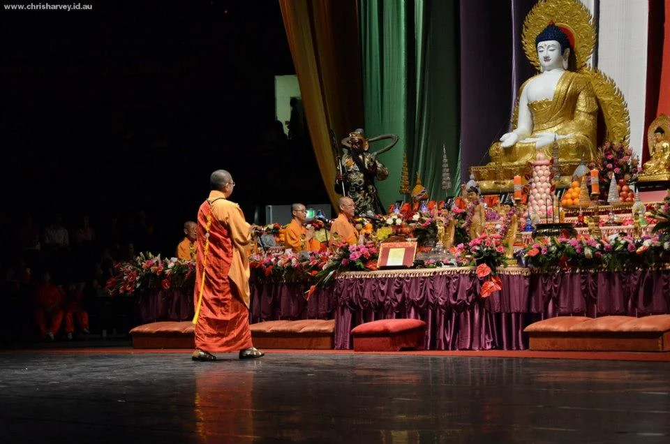 He crossed the stage alone, orange against deep shadow, the Buddha watching from behind. I had one frame at the right moment.