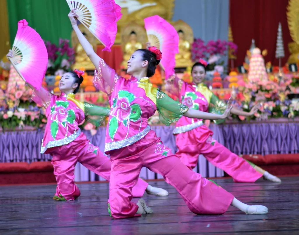 The fan raised above her head, smile fully open, the altar behind her lit in warm gold. This is what the festival looks like when it is working.