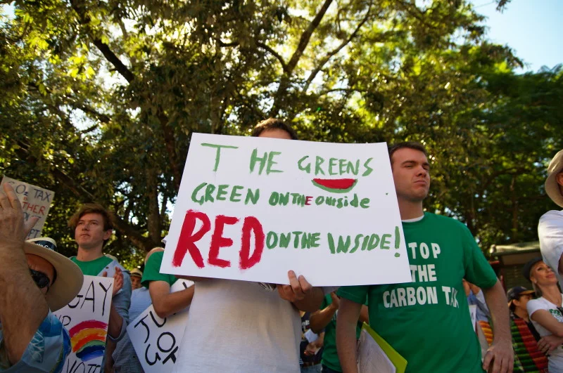 The sign says 'green on the outside, red on the inside.' The person behind it is obscured. The sign is the portrait.