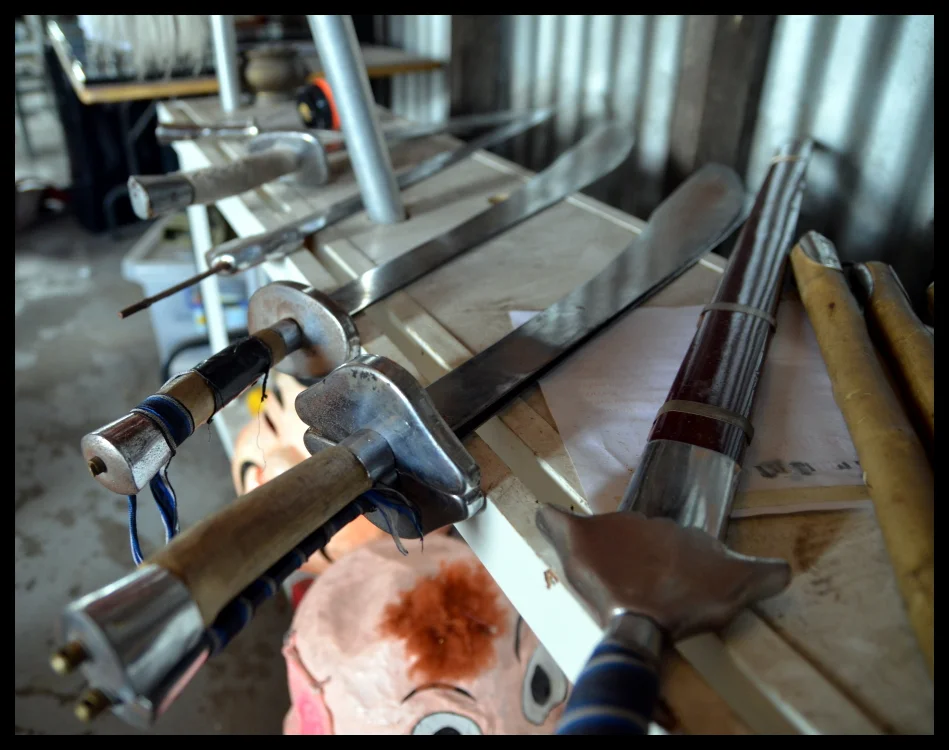Swords and weapons laid out on the workbench before the performance. Blades and handles and the lion mask in the background. The equipment of ceremony.